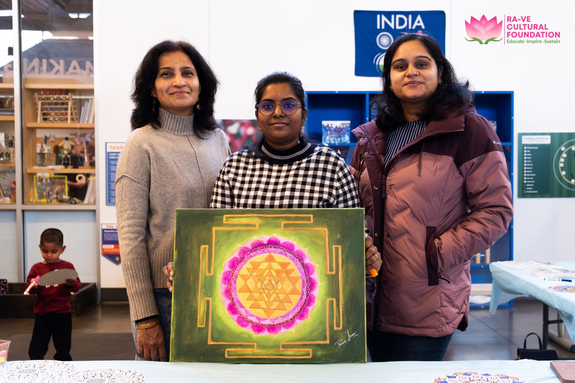 Group of women smiling together in front of a white board with drawings on a yellow wall.