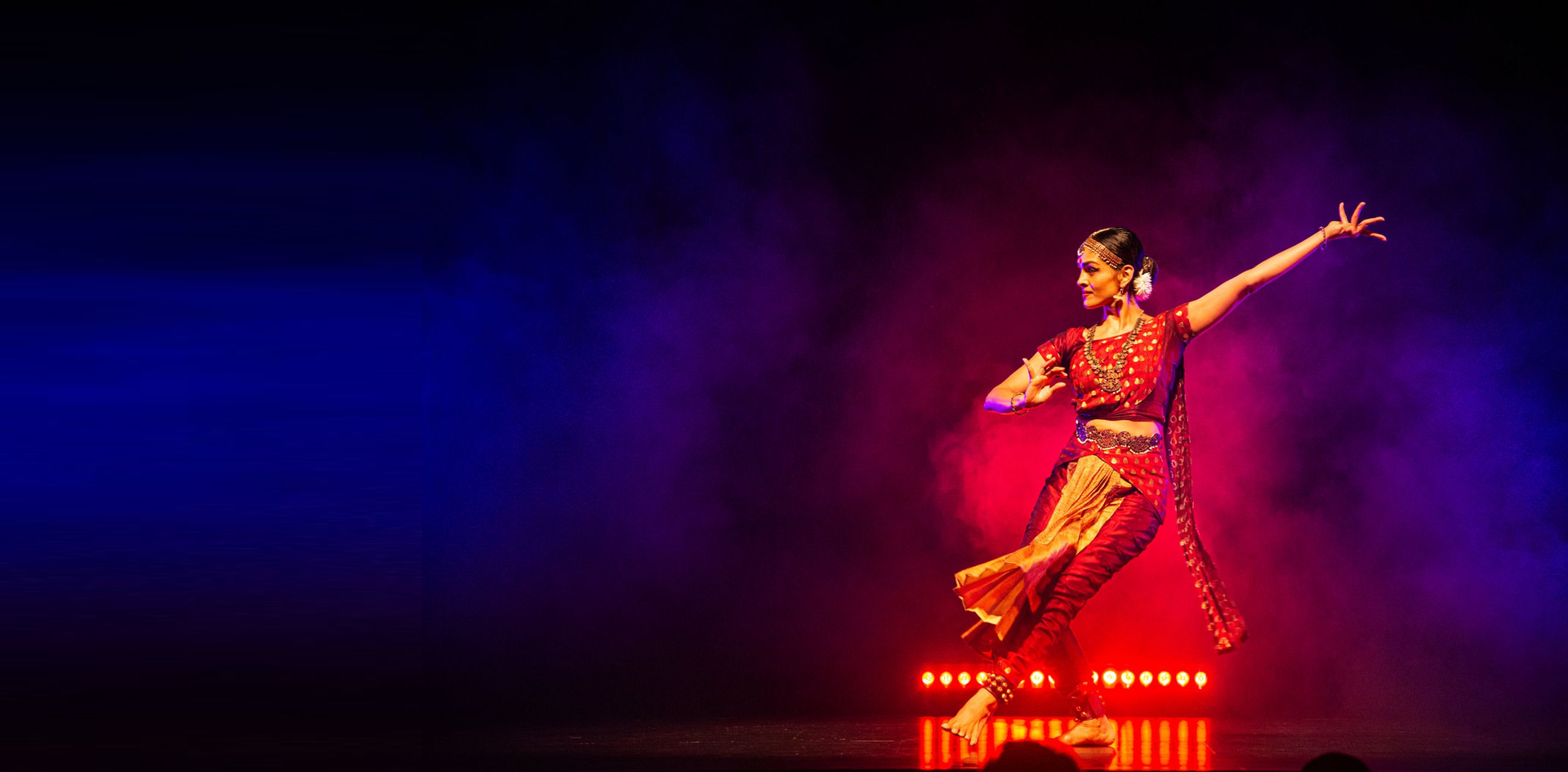 Woman in red costume performing a traditional dance on stage, with red and blue lighting.