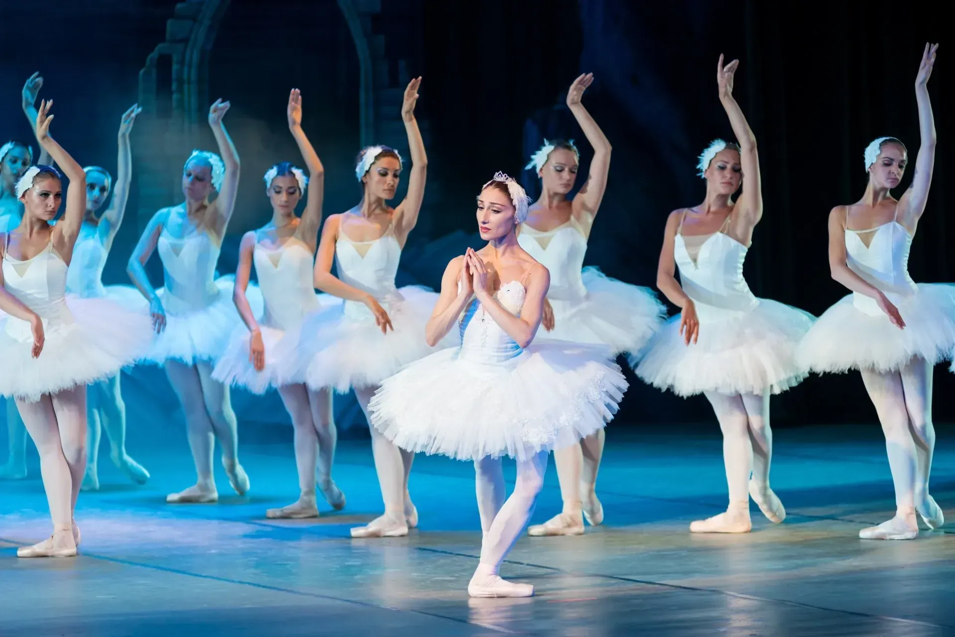 Ballet dancers in white tutus and headdresses performing on stage.