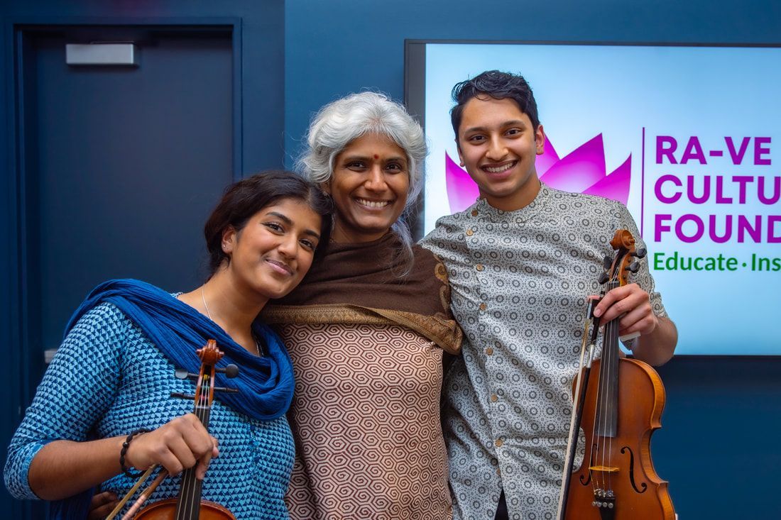 Three people smiling with violins, in front of a blue wall and a sign that reads
