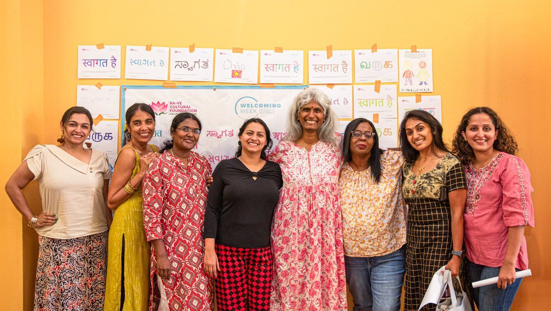 Group of women smiling together in front of a white board with drawings on a yellow wall.