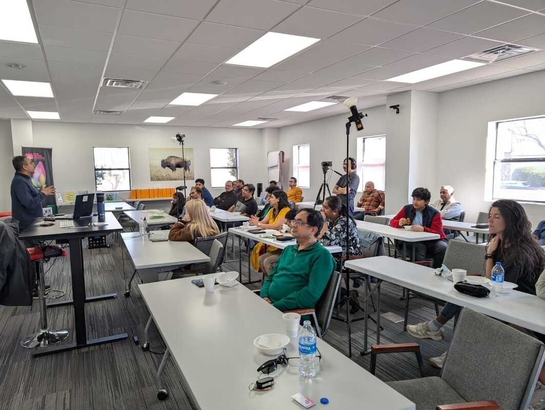 Classroom lecture in progress, presenter at lectern. Attendees sit at desks, some facing the front.