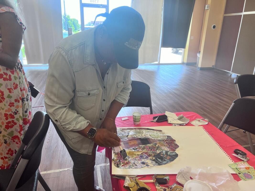 Person wearing a cap, focused on creating art on a table in a brightly lit room.