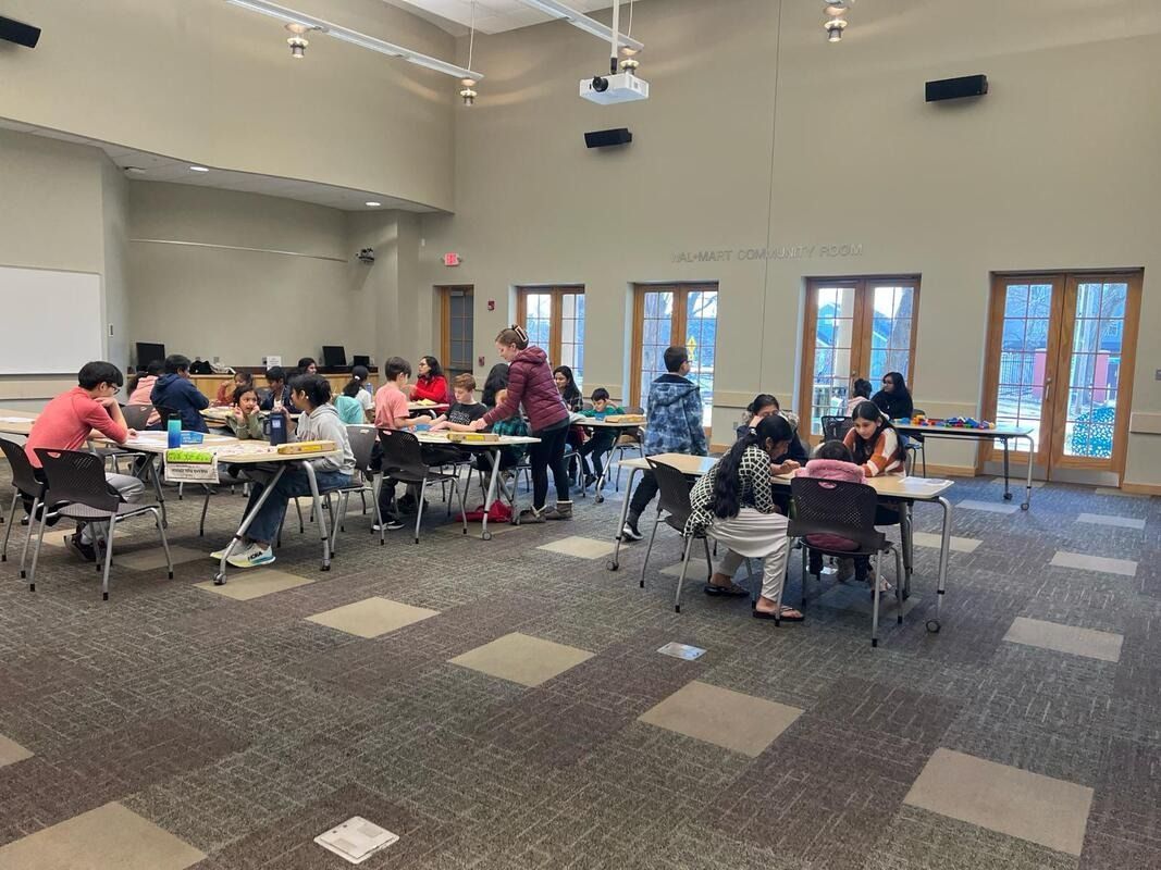 People working at tables in a large room with windows and a projector.