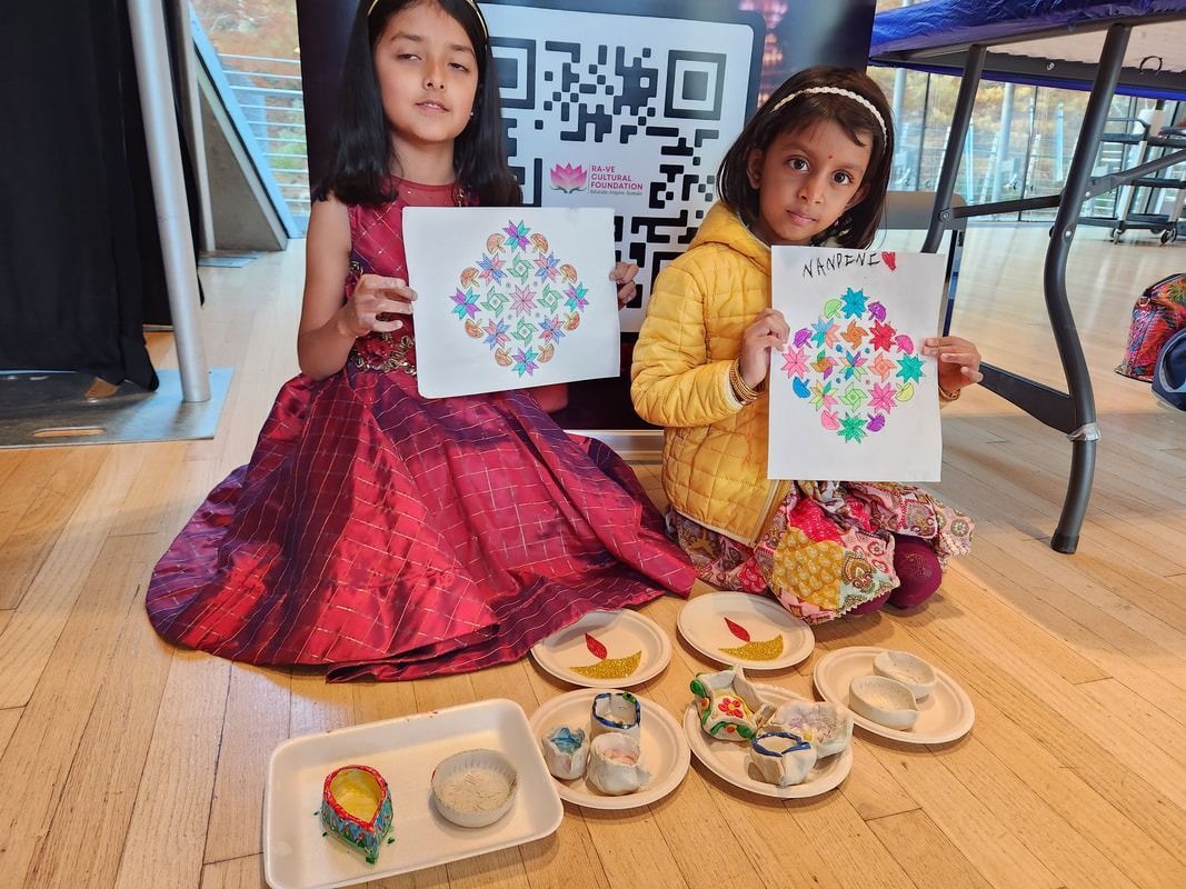 Two girls holding colorful artwork, sitting on floor with crafts and candles.