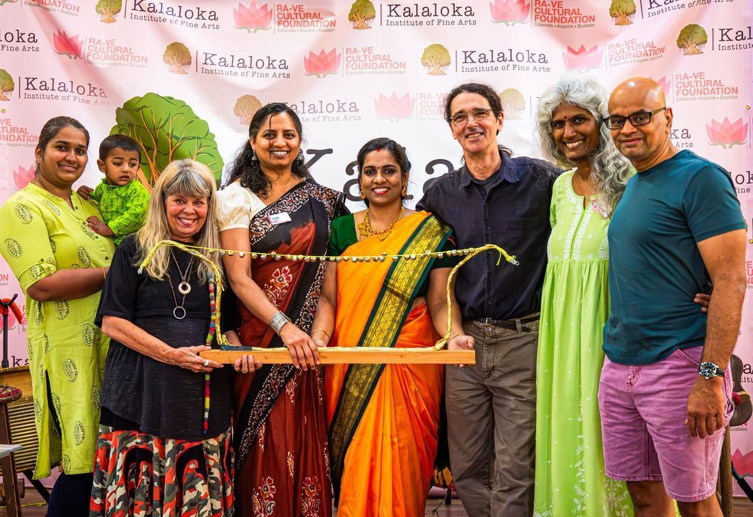 Group of people holding a decorated wooden rod, smiling in front of a banner.