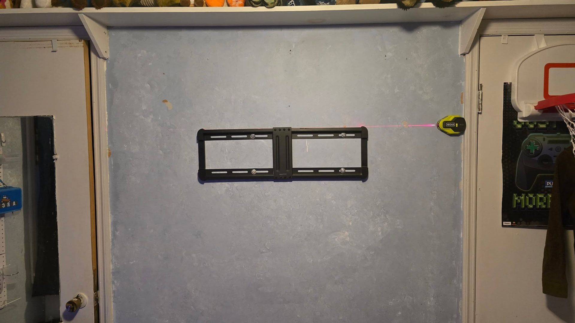 Gray wall with a black two-slot bracket mounted in the center, framed by shelves and hanging items.