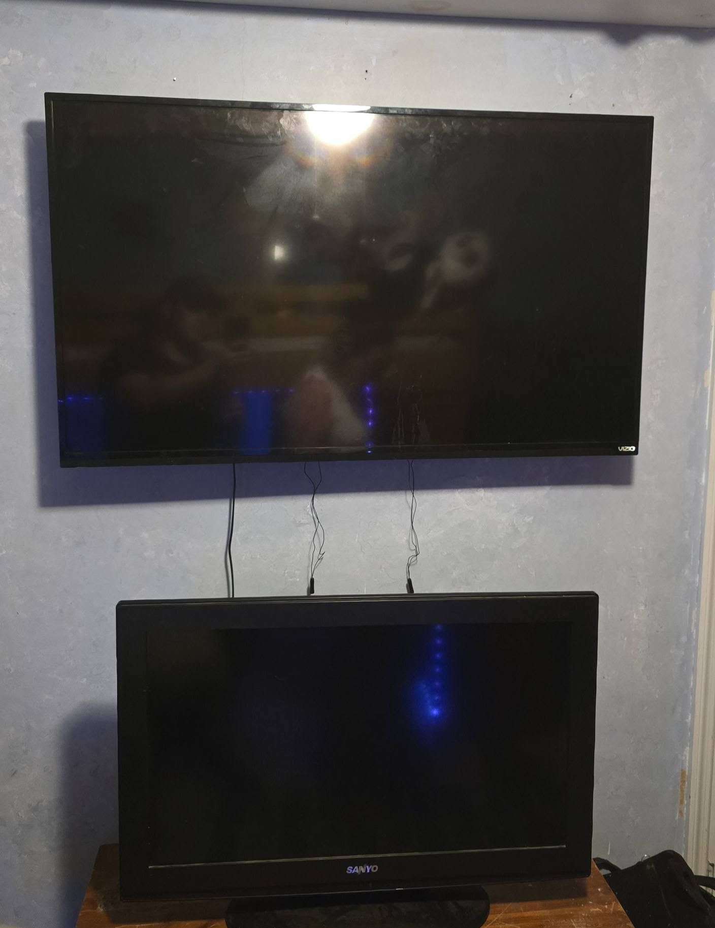 Two flat-screen TVs mounted one above the other on a gray wall, both turned off.