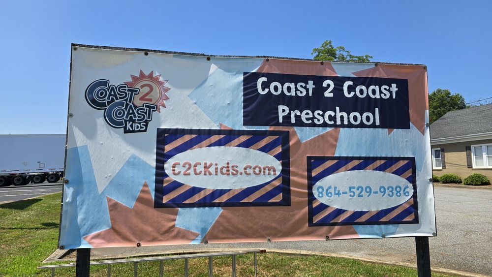 Coast 2 Coast Preschool banner with logo, website, and phone number on a grassy roadside
