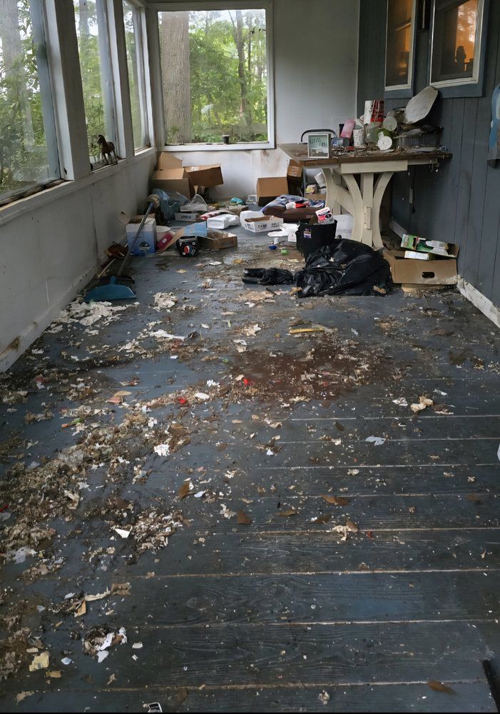 Messy porch with scattered leaves, trash, and a black bag beside a small table and windows.