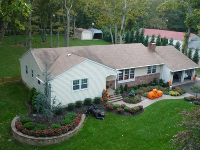 Aerial view of a white house with a landscaped front yard, flower beds, and pumpkins near the porch.