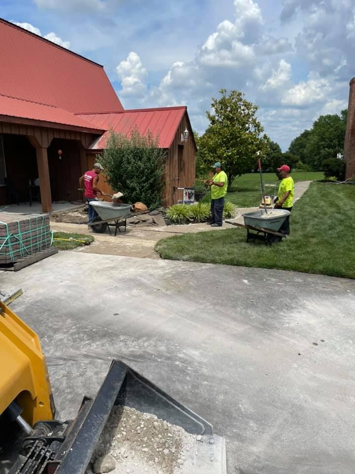 Three men are pushing wheelbarrows in a driveway in front of a building.