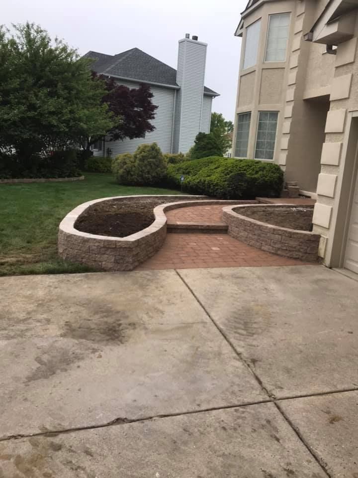 A concrete walkway leading to a house with a brick wall and steps.