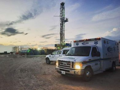 Una ambulancia y un camión estacionados cerca de una plataforma petrolera al anochecer.