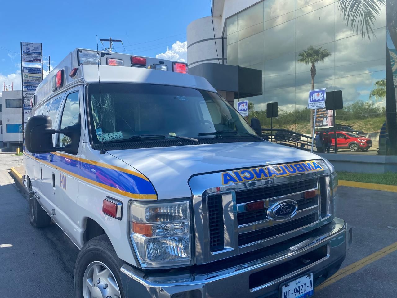 Ambulancia blanca estacionada frente a un edificio, con luces intermitentes.