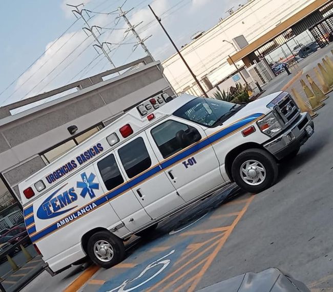 Ambulancia blanca con detalles en azul y rojo estacionada al aire libre. Se ven las palabras
