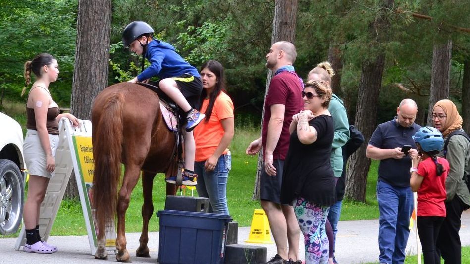 Un groupe de personnes se tient autour d'un cheval avec un enfant qui le monte.