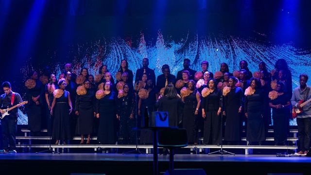 Une chorale se produit sur une scène avec un homme jouant de la guitare en arrière-plan