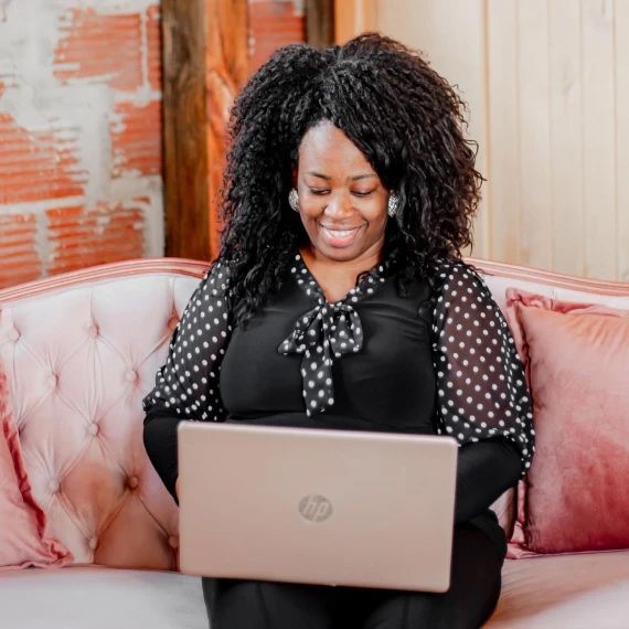 A woman is sitting on a pink couch using a laptop computer.