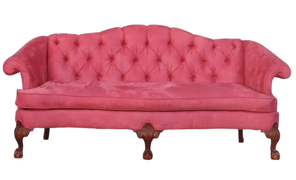 A pink tufted couch with wooden legs on a white background.