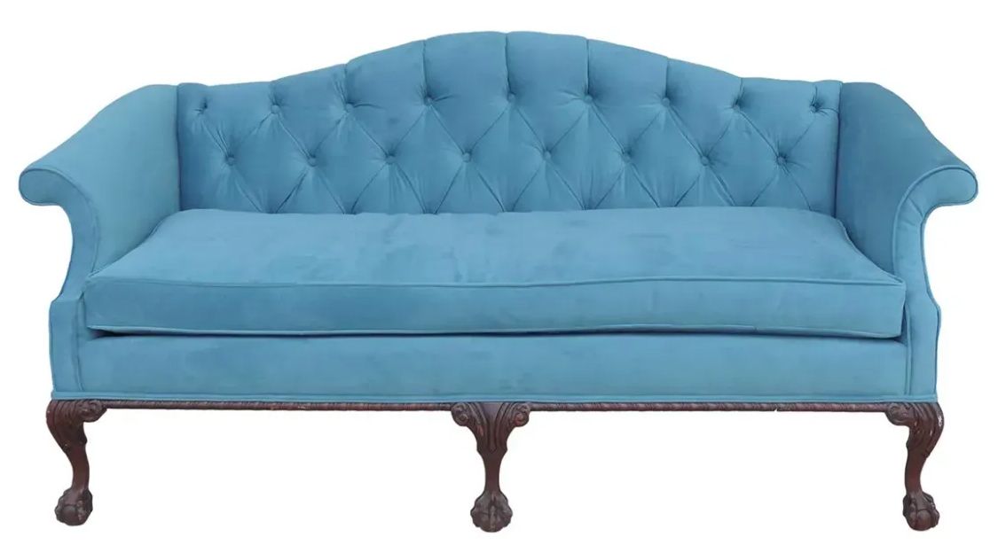A blue tufted couch with wooden legs on a white background