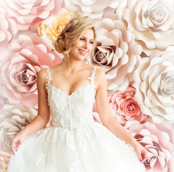 A woman in a wedding dress is standing in front of a wall of roses