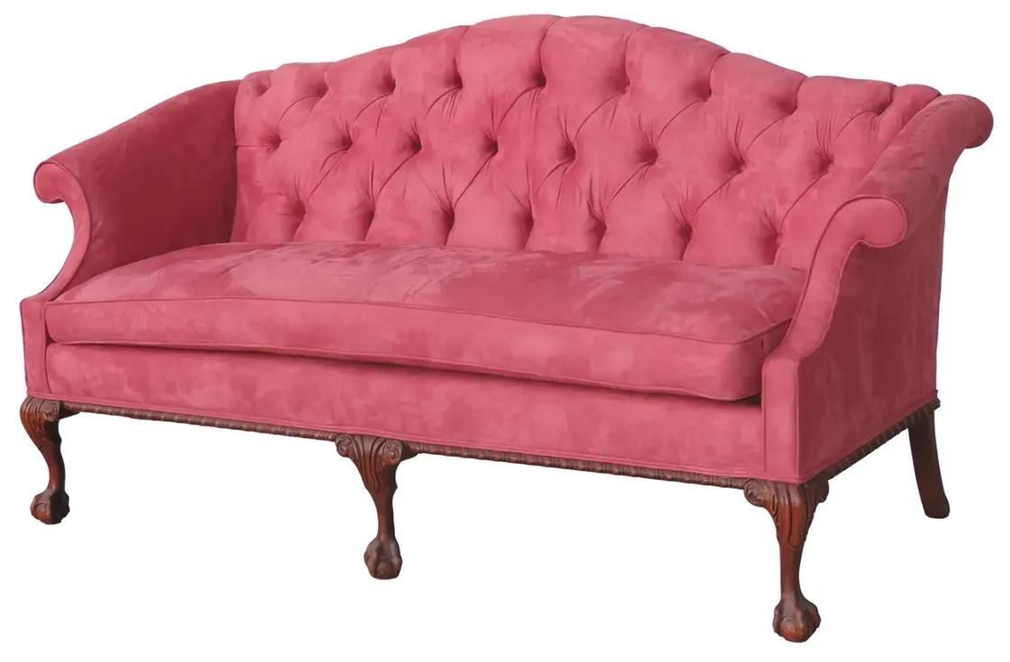 A pink tufted couch with wooden legs on a white background
