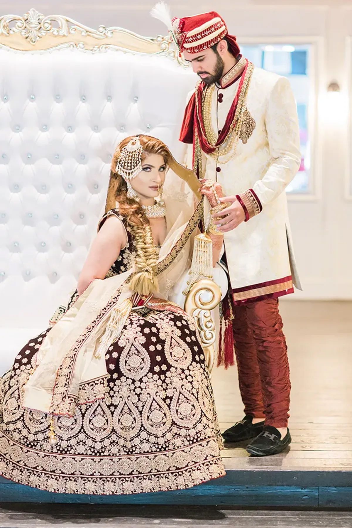 A bride and groom are posing for a picture while the bride is sitting on a couch.