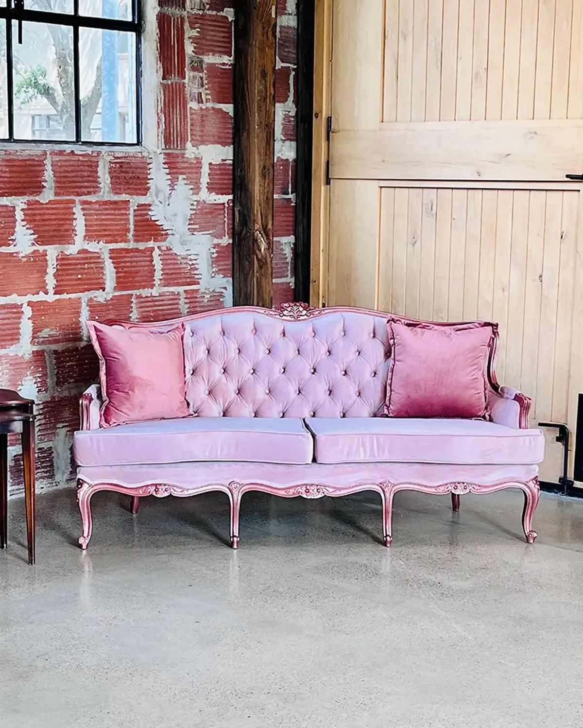 A pink couch is sitting in front of a brick wall