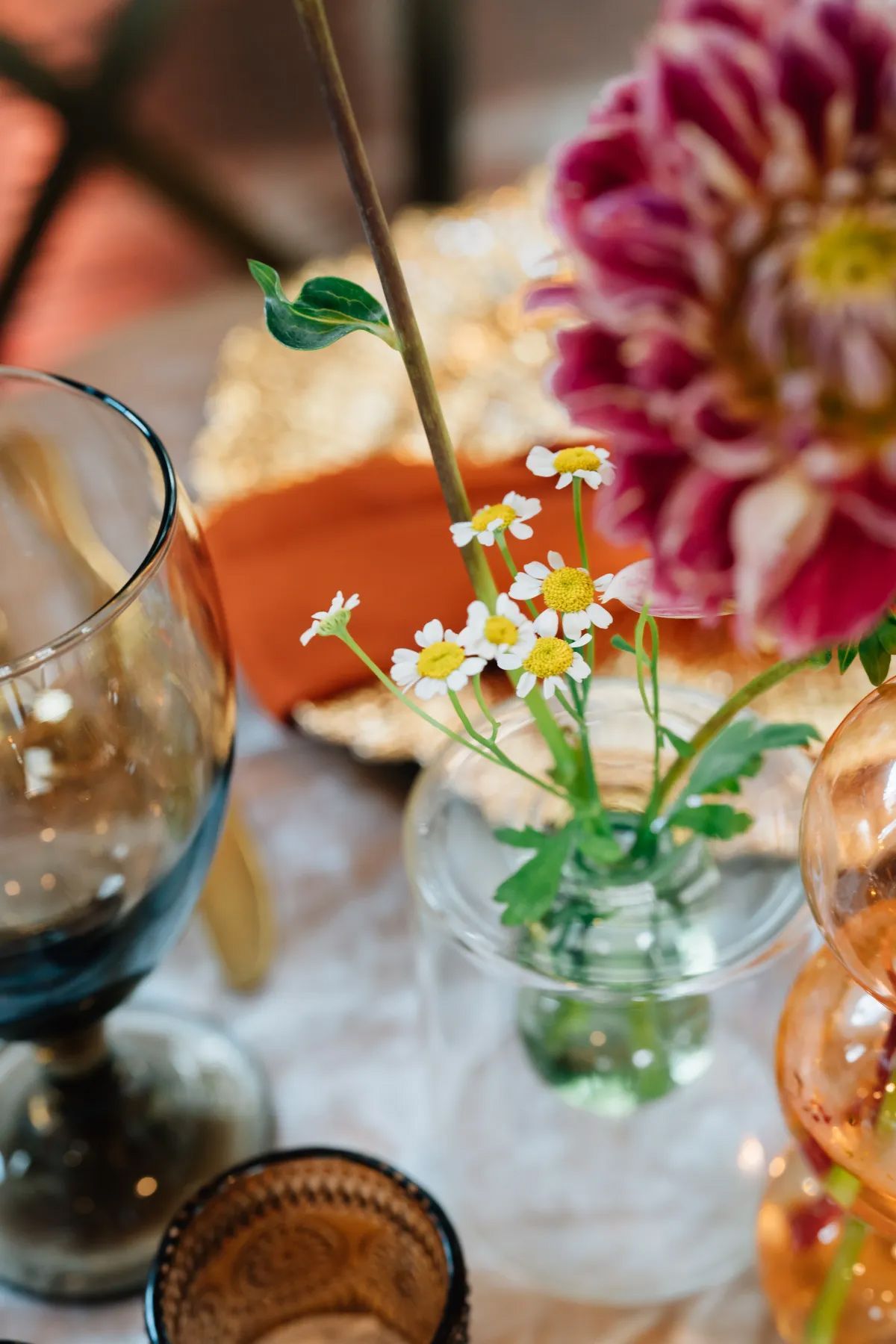 A vase filled with daisies and a glass of wine on a table.