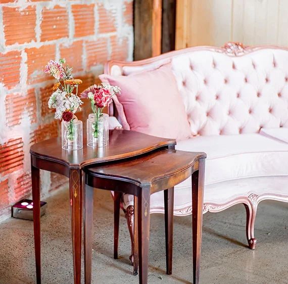 A pink couch is sitting next to two tables with vases of flowers on them.