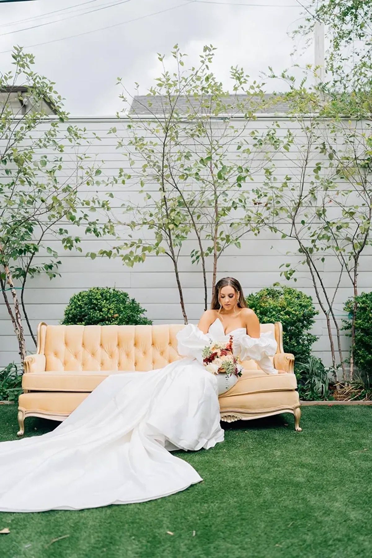A bride in a wedding dress is sitting on a couch in a garden.