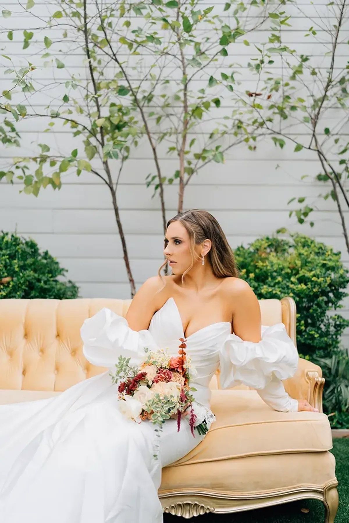 A bride in a white dress is sitting on a couch holding a bouquet of flowers.