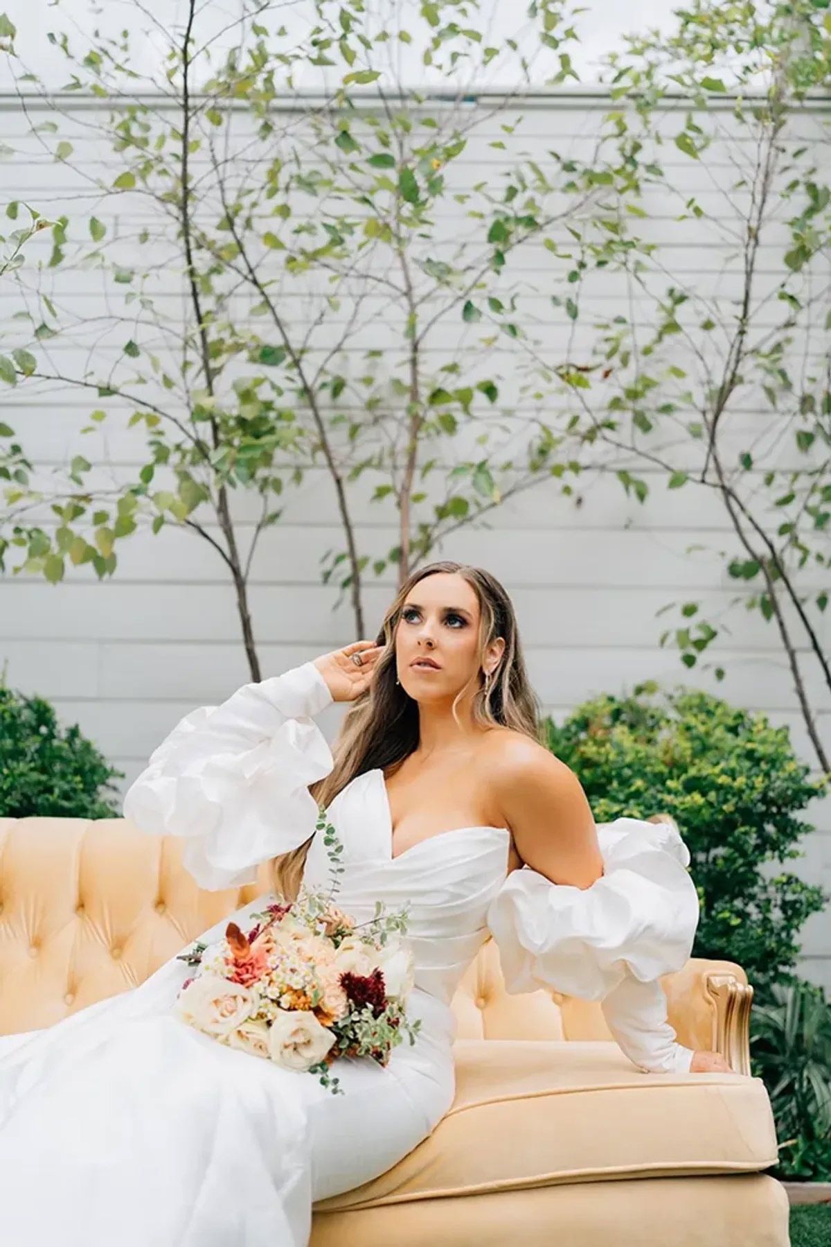 A bride in a white dress is sitting on a couch holding a bouquet of flowers.