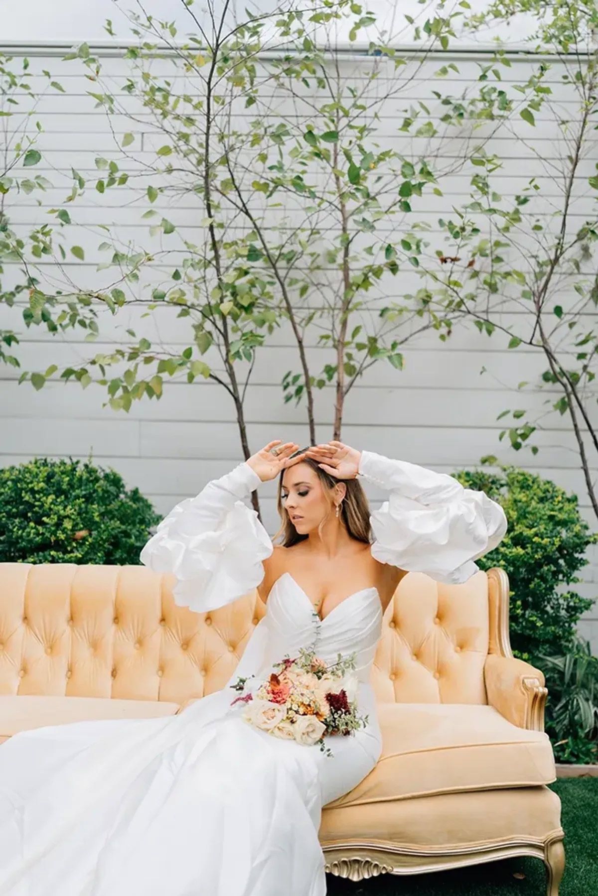 A bride in a white dress is sitting on a couch holding a bouquet of flowers.