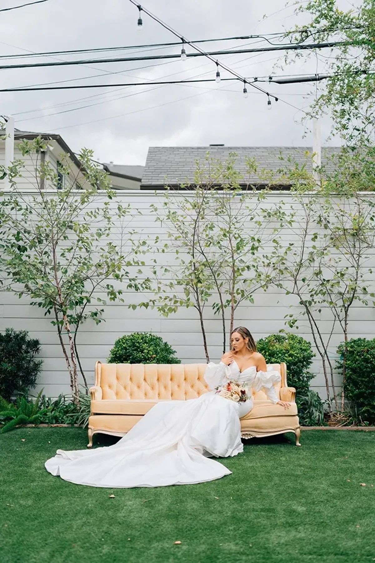 A bride in a wedding dress is sitting on a couch in a backyard.
