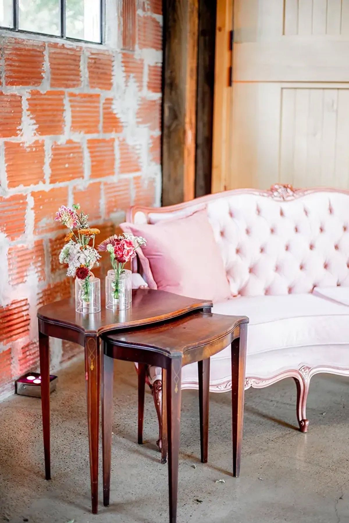 A pink couch is sitting next to two tables with vases of flowers on them.