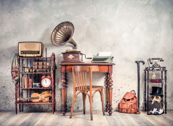 A room with a desk , chair , record player , clock , radio and other antique items.