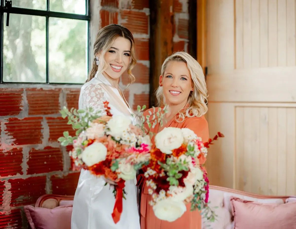 Two women are standing next to each other holding bouquets of flowers.