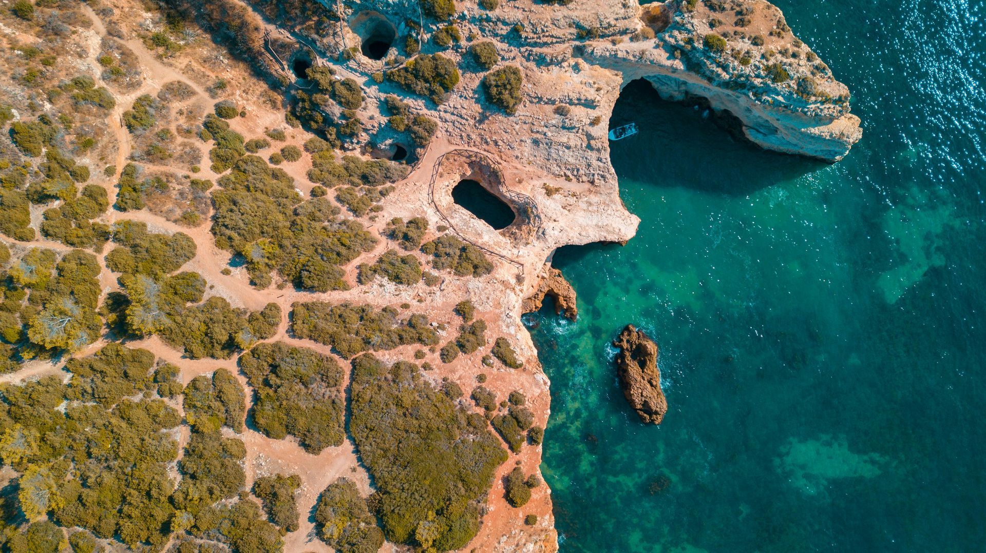 An aerial view of a cliff overlooking the ocean with a boat in the water.