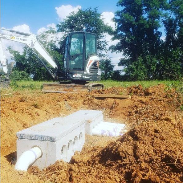 A small excavator is sitting in the dirt next to a concrete box.