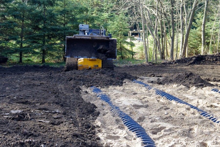 A bulldozer is moving dirt in a field with trees in the background.