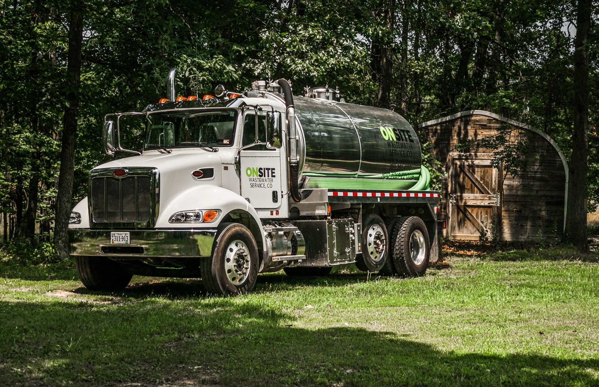 A white and green vacuum truck is parked in a grassy field.