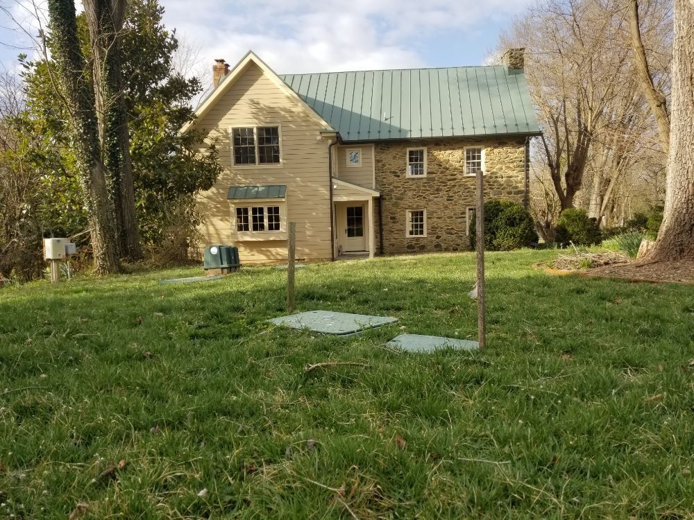 A large house with a green roof is sitting in the middle of a lush green field.