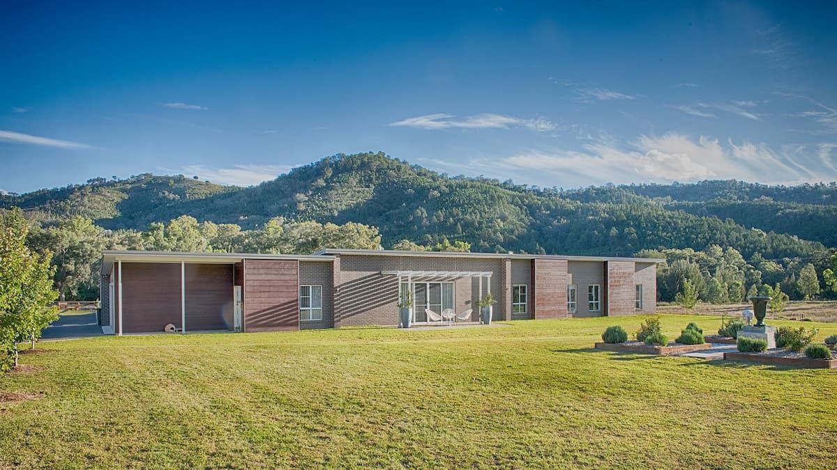 A Large House Is Sitting In The Middle Of A Grassy Field With Mountains In The Background — D&C Projects in Nelson Bay, NSW