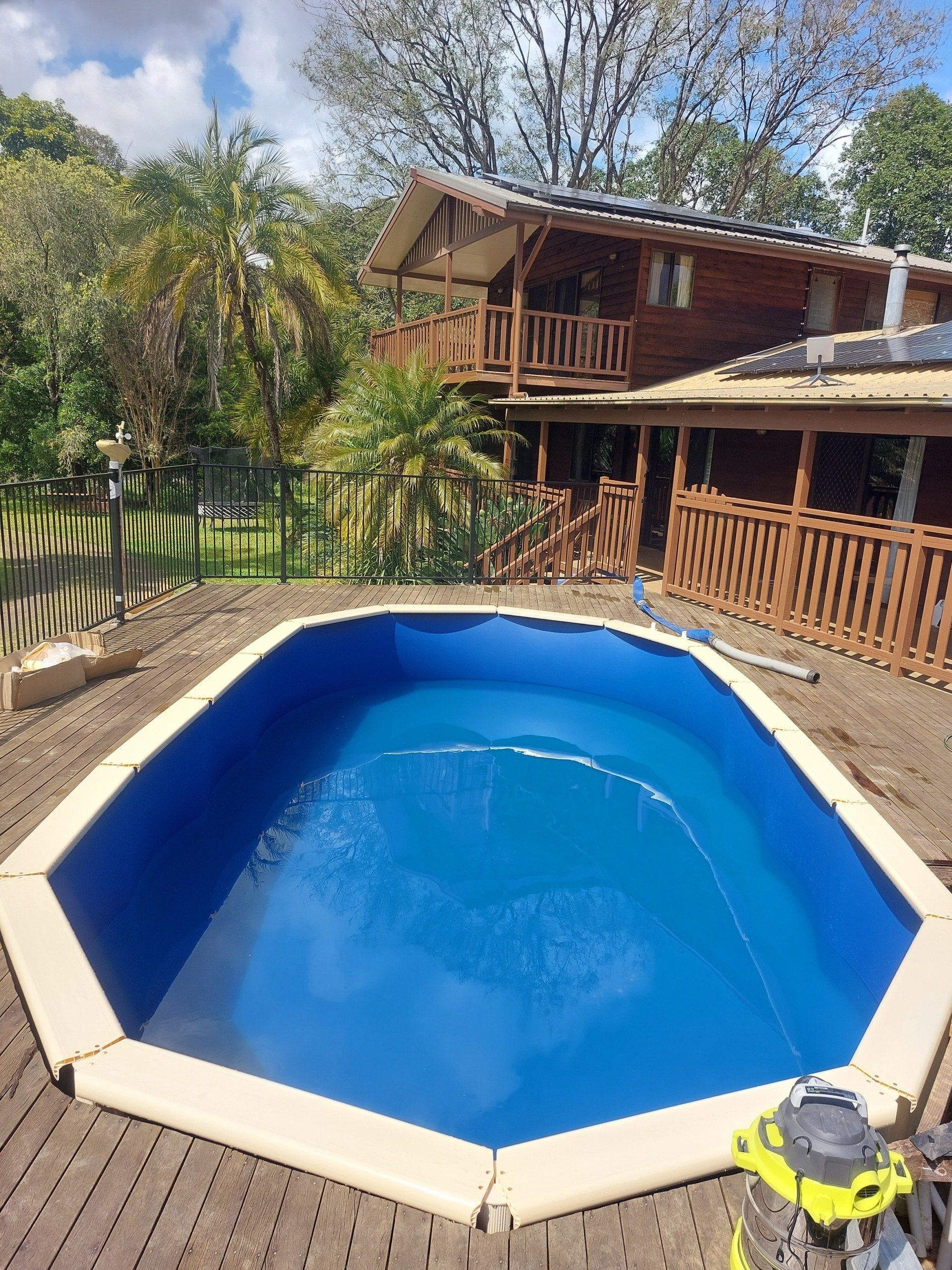 A large swimming pool is sitting on top of a wooden deck in front of a house.