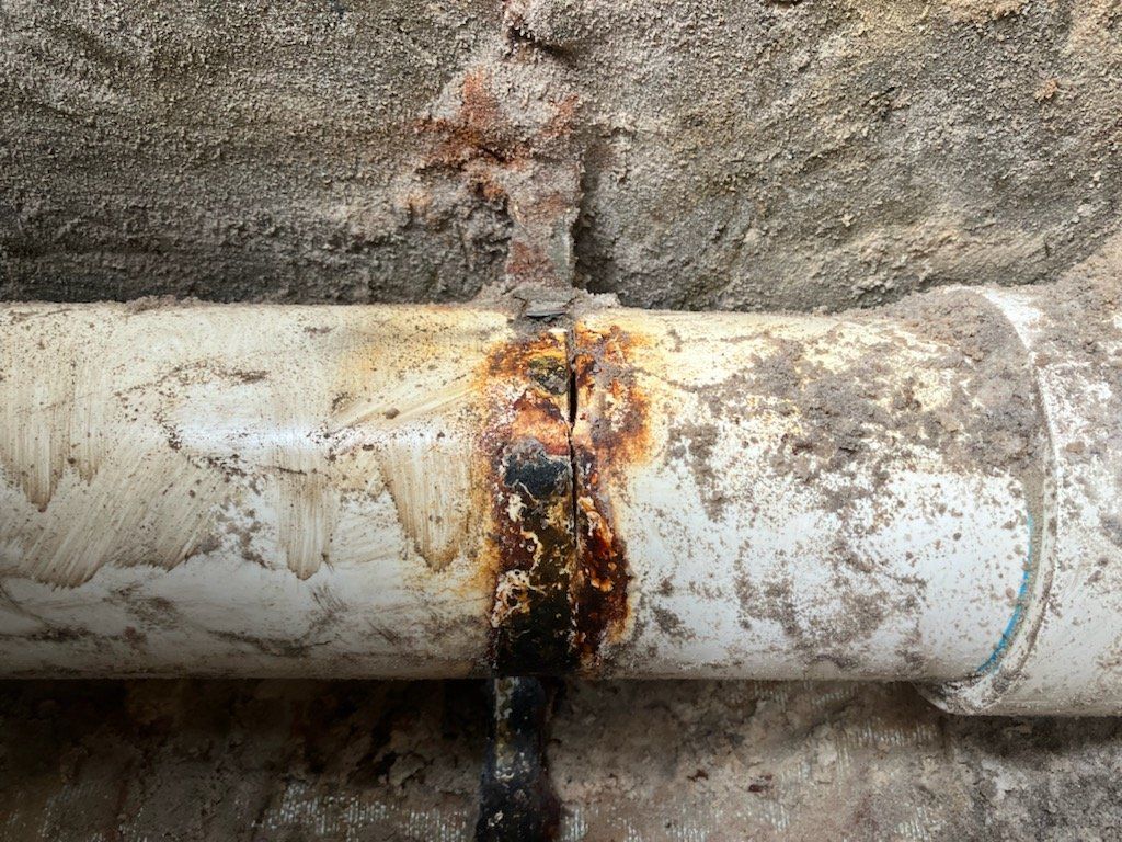 A close up of a rusty pipe against a concrete wall.