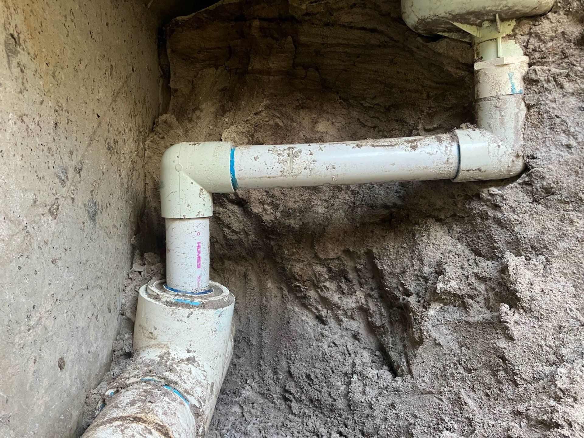 A white pipe is connected to a concrete wall.