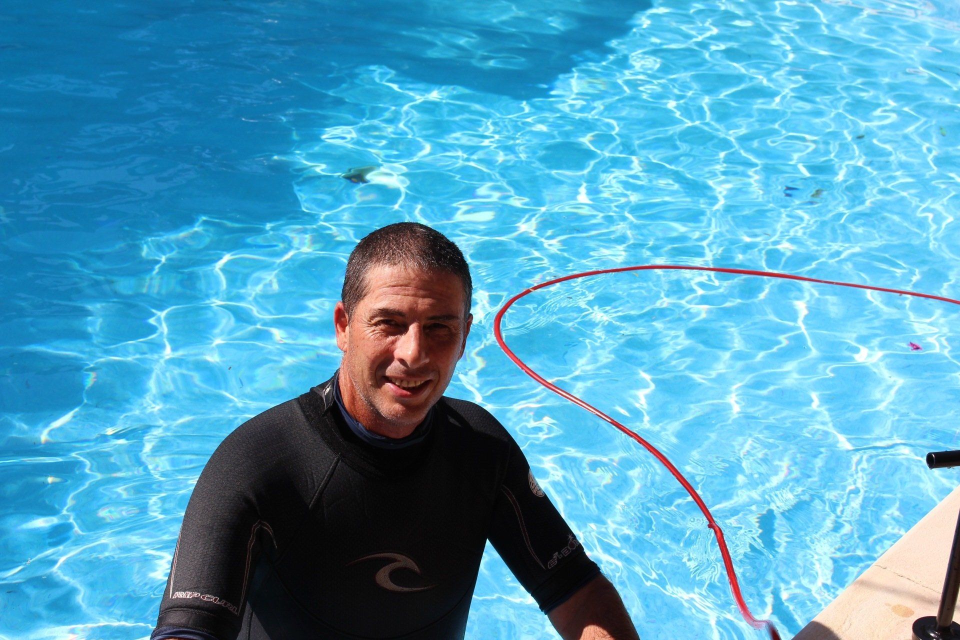 A man in a wetsuit is standing next to a swimming pool