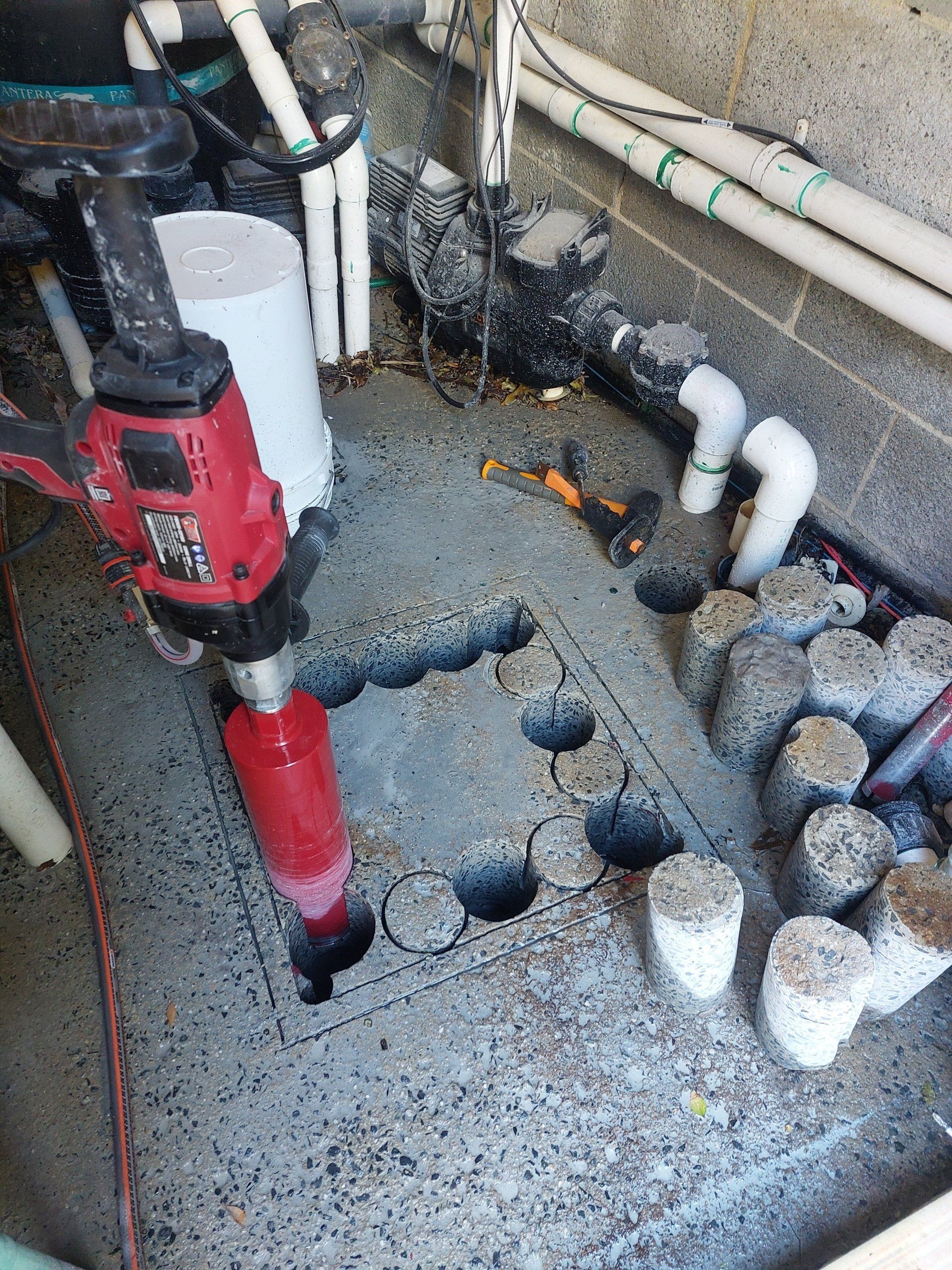 A red drill is cutting holes in a concrete floor.